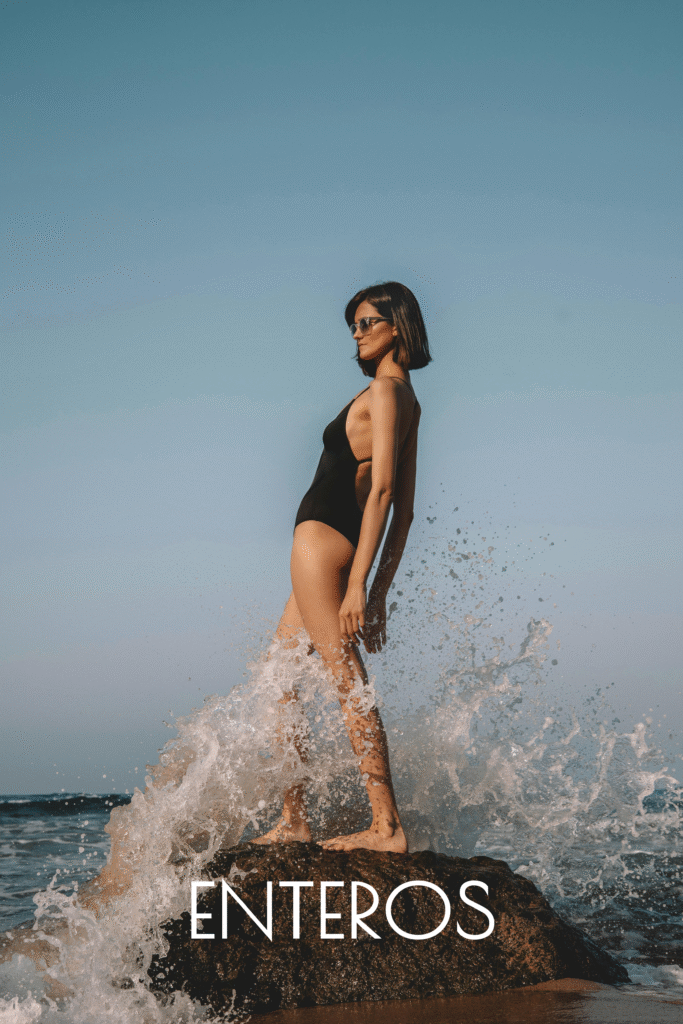 mujer encima de una roca chocando las olas del mar y con un bañador negro