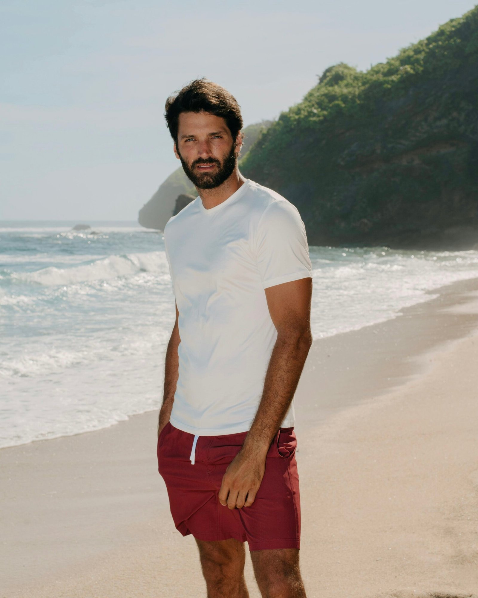 hombre en la playa con bañador granate de kou y camiseta blanca